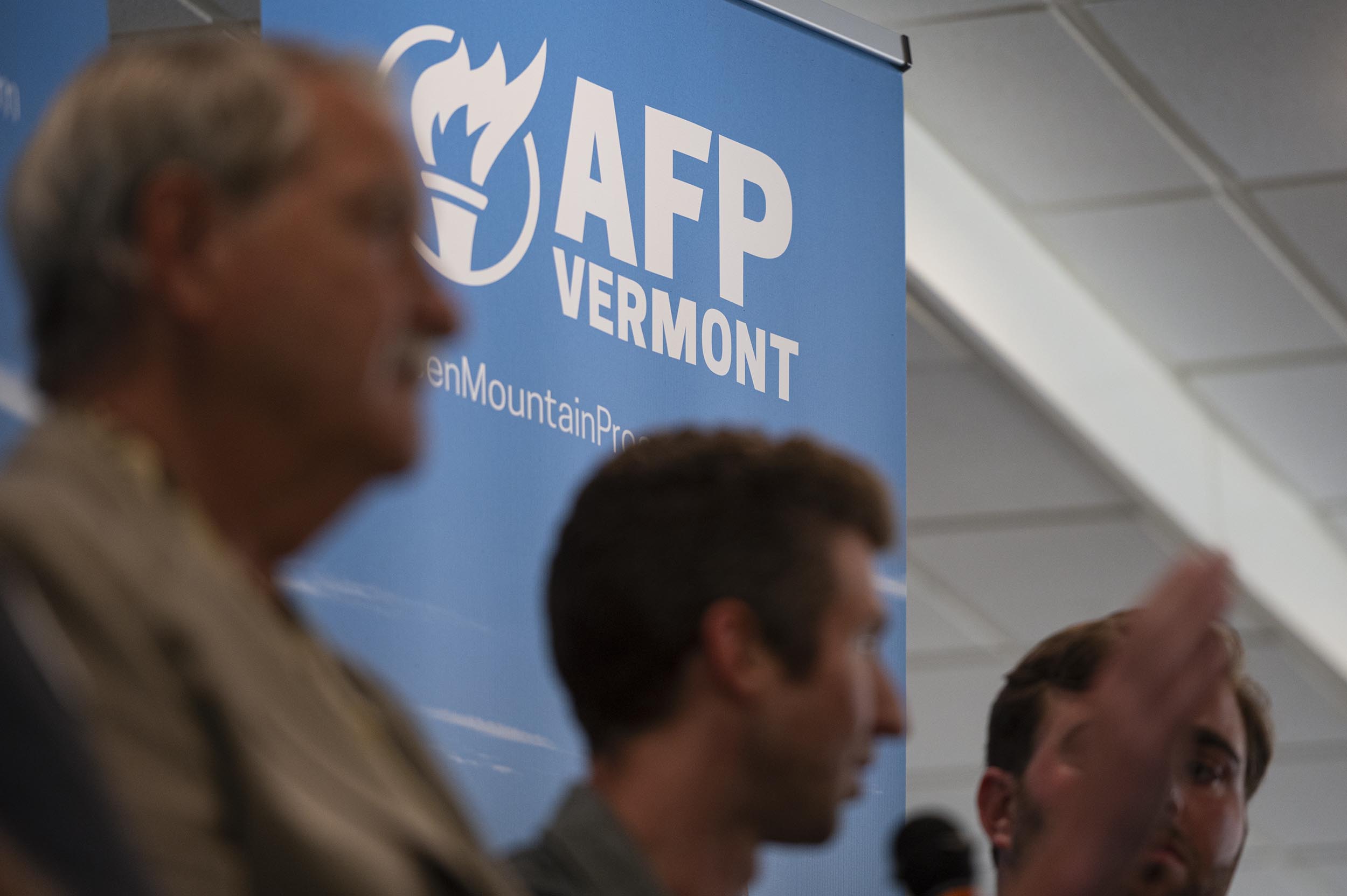 Three men sit in front of a blue "AFP Vermont" banner during an indoor event or panel discussion.