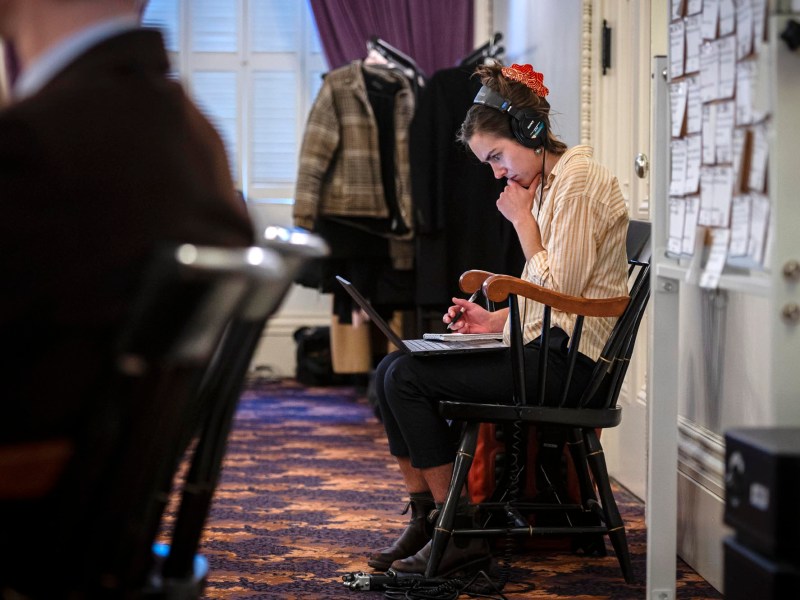 A woman sitting in a chair with headphones on her chin and a laptop.