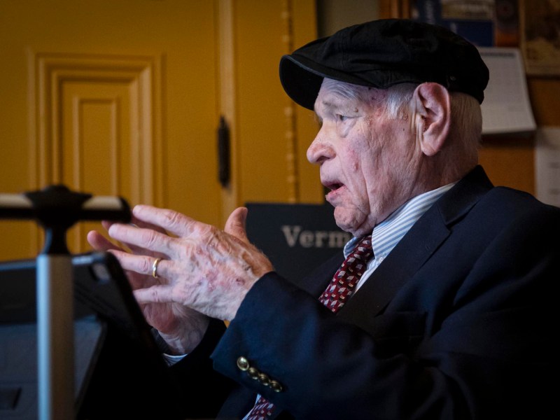An older man in a suit and tie talking on a laptop.