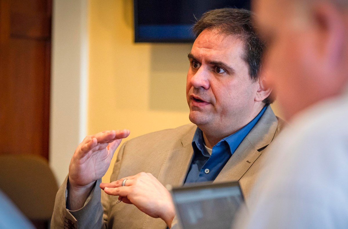 Man in a gray suit gesturing while speaking to another person.