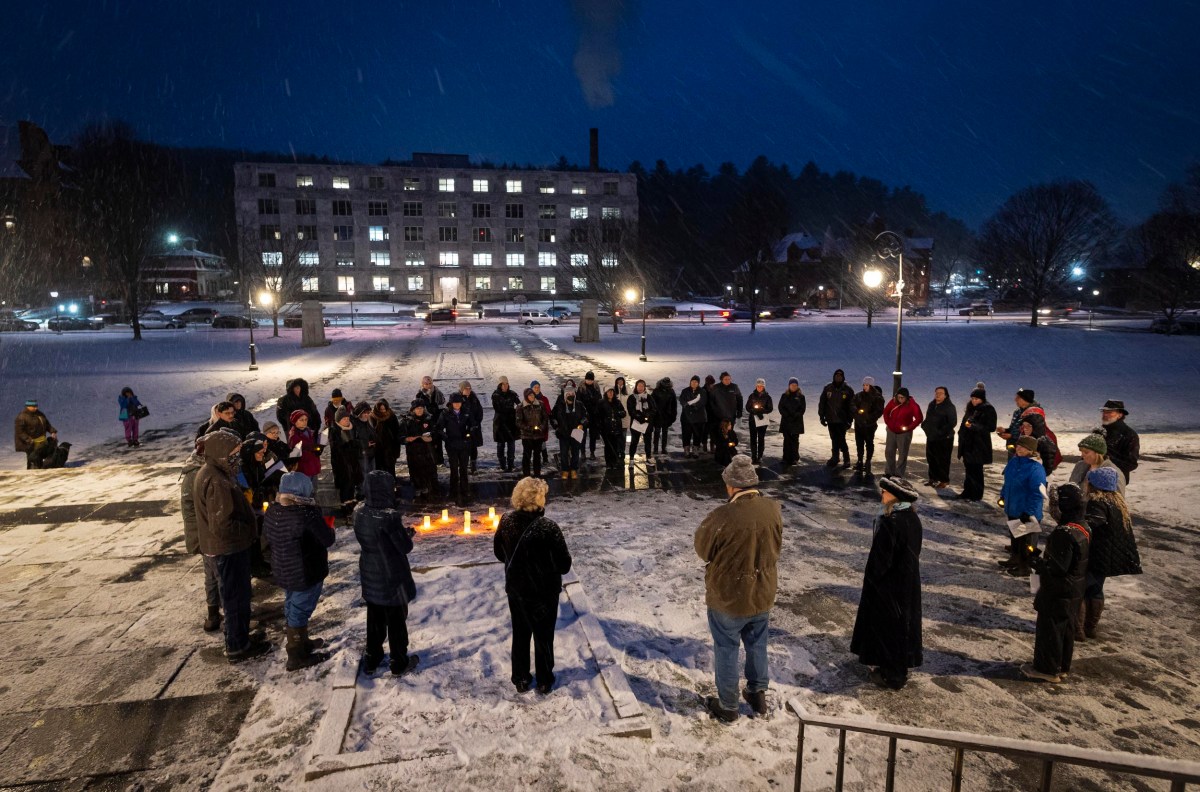 A group of people standing in a circle around lit candles on a snowy evening, in front of an illuminated building.