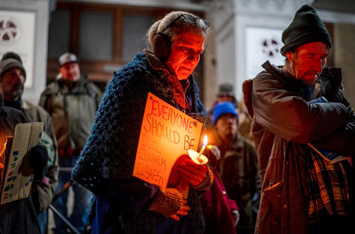 A group of people holding candles, with one person wearing a sign that reads, "Everyone should be warm and safe.