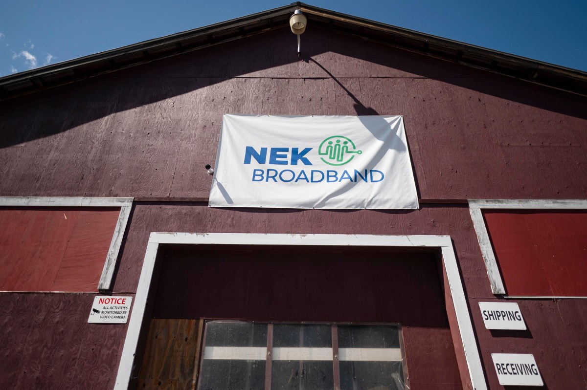 A large sign reading "NEK Broadband" is displayed above the entrance of a brown warehouse with shipping and receiving signs by the door.