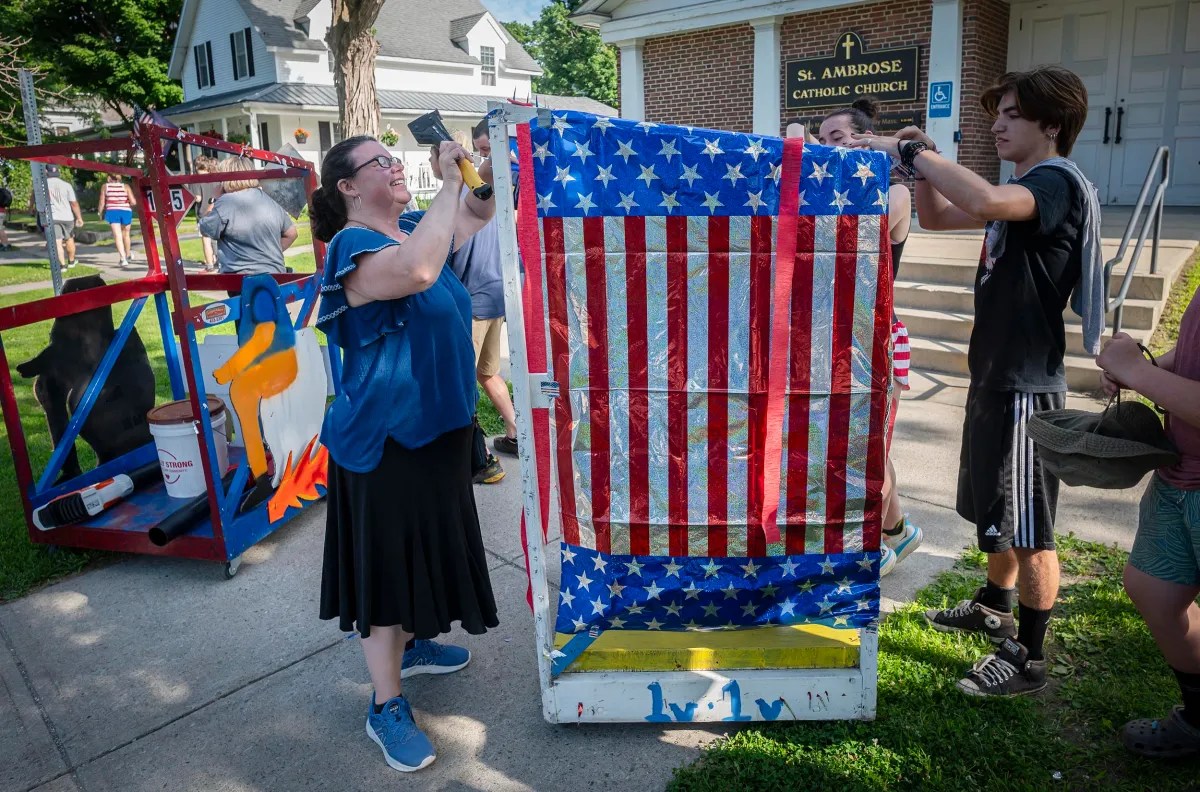 People decorating a cart with an American flag pattern outside a church. A woman is stapling the fabric while others assist her.
