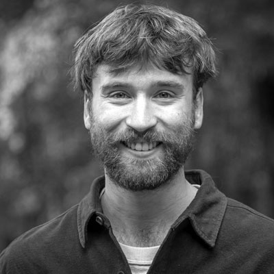 A man with a beard and short hair smiles at the camera, wearing a dark shirt. The background is blurred.