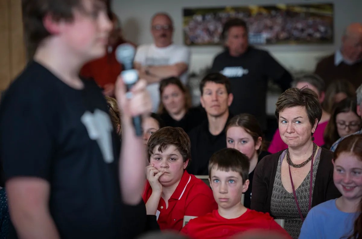 A speaker addressing an attentive audience, with focus on a woman in the center who is listening intently.