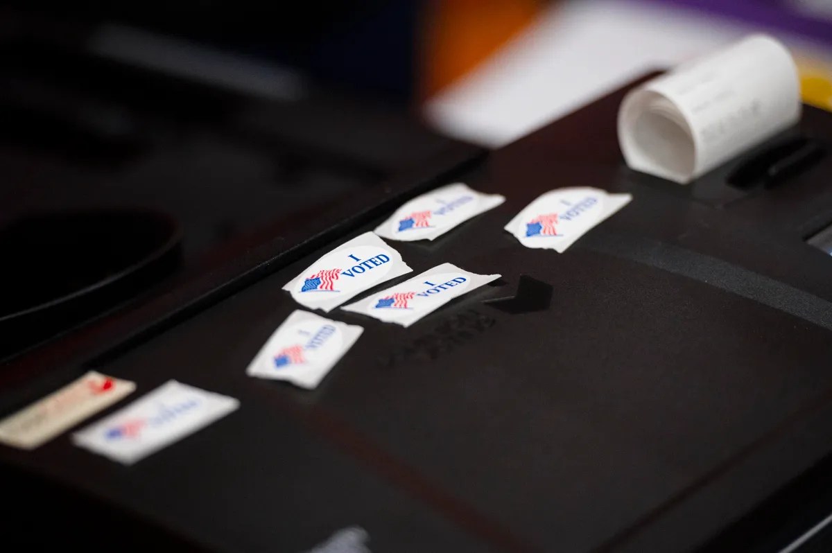 I Voted" stickers on a dark surface next to a small roll of paper.