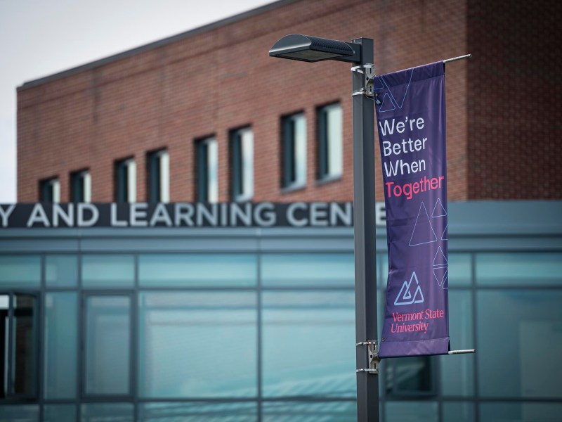 A banner reading "We’re Better When Together" hangs on a lamp post in front of a building labeled "Library and Learning Center" at Vermont State University.