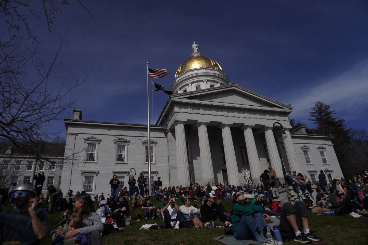 People gathered on the lawn of a state capitol with a golden dome under a clear blue sky.